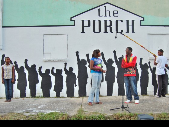 A shot of The Porch's mural shows sillohuettes of children as 3 real life children perform