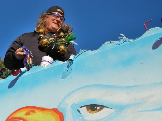 Krewe rider with fistful of beads atop seagull float